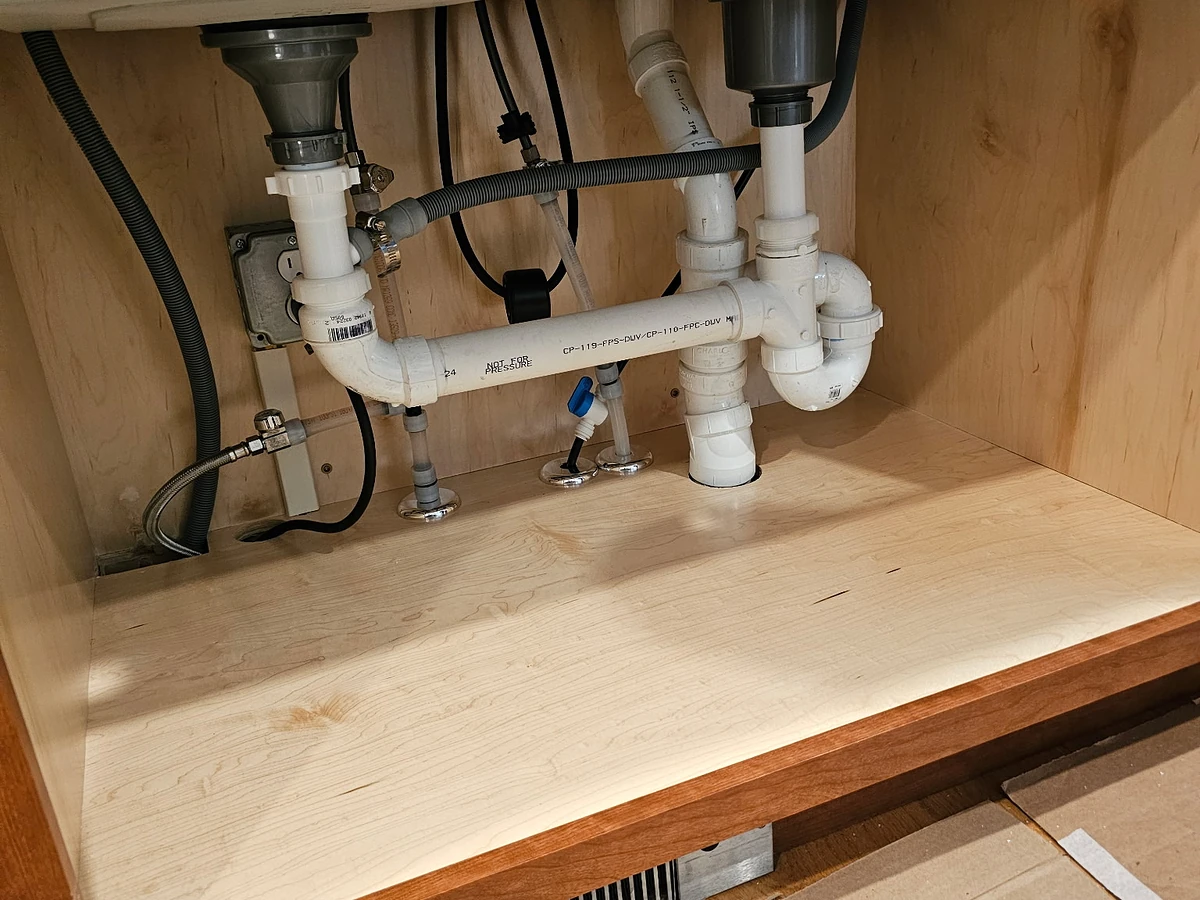 Under-sink plumbing replacement under a double-bowl kitchen sink with new PVC trap and supply valves by A.J. LeBlanc Heating licensed plumbers in a Southern NH home